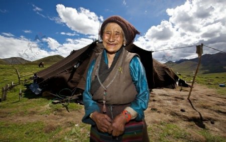 蓝天白云下草原上的藏族老奶奶图片