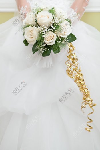 白色婚纱上拿着捧花的新娘的手图片