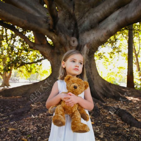 大树下抱着布娃娃的可爱小女孩图片