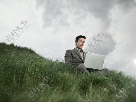 草地上玩电脑的男人图片