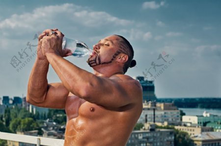 蓝天下喝水的肌肉男人图片
